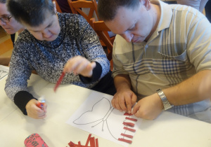 Kilka osób wykonuje prace plastyczną z kolorowych pasków papieru.