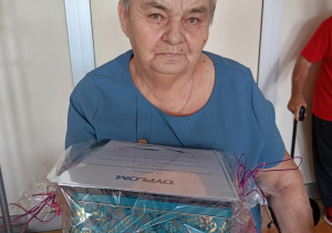 Kobieta w niebieskiej bluzce trzyma w ręku dyplom.