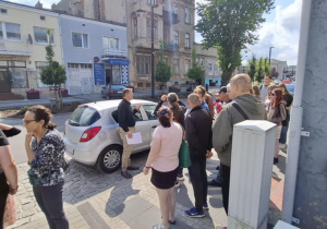 Grupa osób stojących na chodniku w mieście.