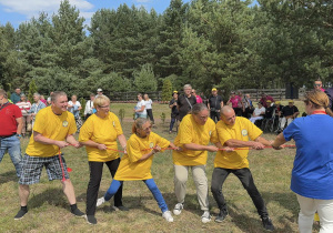 Grupa osób ubranych w żółte koszulki przeciąga linę.