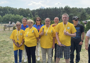 Grupa osób w żółtych koszulkach pozuje do zdjęcia. Na szyi mają zawieszone medale.