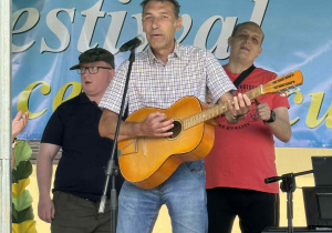 Trzech mężczyzn występujących na scenie. Jeden z mężczyzn gra na gitarze.