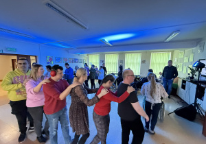 Grupa osób tańczy trzymając się za ramiona.