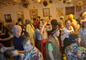 Duża grupa osób w różnych przebraniach tańczy na balu karnawałowym.