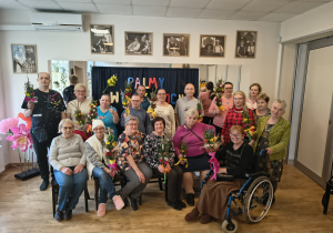 Zdjęcie grupowe osób, które brały udział w warsztatach. osoby na zdjęciu w rękach trzymają wykonane przez siebie kolorowe palmy wielkanocne.