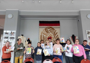 Grupa osób pozuje do zdjęcia z wykonanymi pracami plastycznymi.