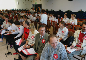 Grupa osób siedzących na krzesłach przygotowywuje się do występu.