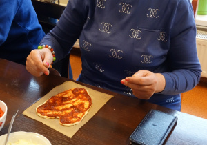 Kobieta siedząca przy stole dekoruje pizzę