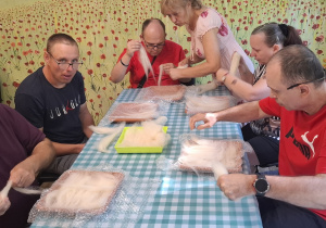 Grupa osób siedzi przy stole. Grupa bierze udział w warsztatach plastycznych.