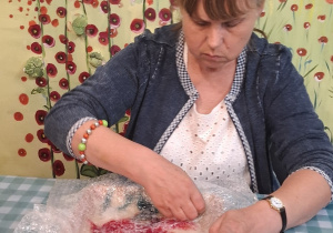 Kobieta siedzi przy stole. Kobieta wykonuje pracę plastyczną.