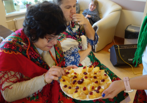 Kobieta ubrana w góralski strój częstuje się oscypkiem.